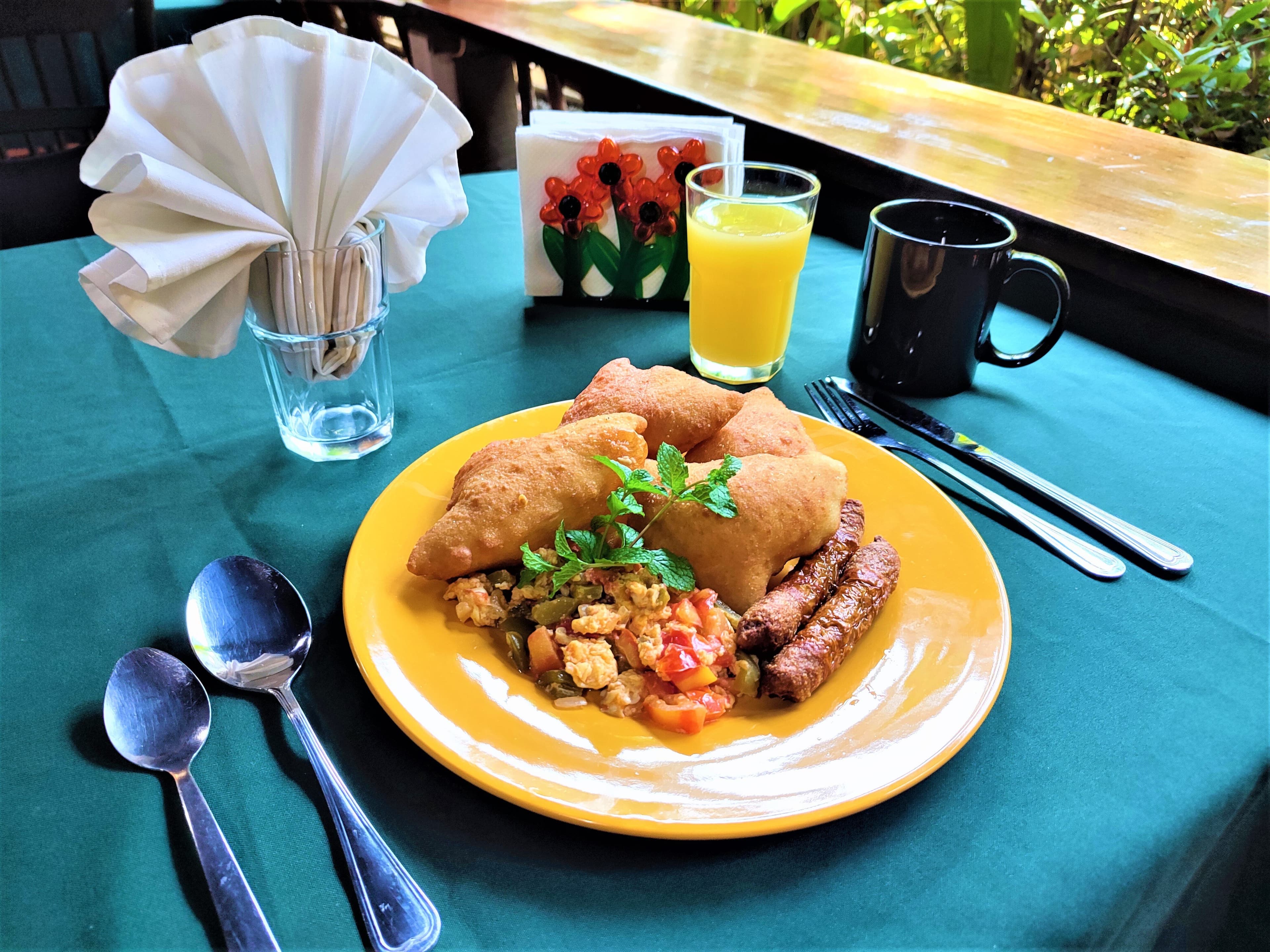 A colorful breakfast plate with stuffed pastries, scrambled eggs, sausage, and drinks on a green tablecloth.